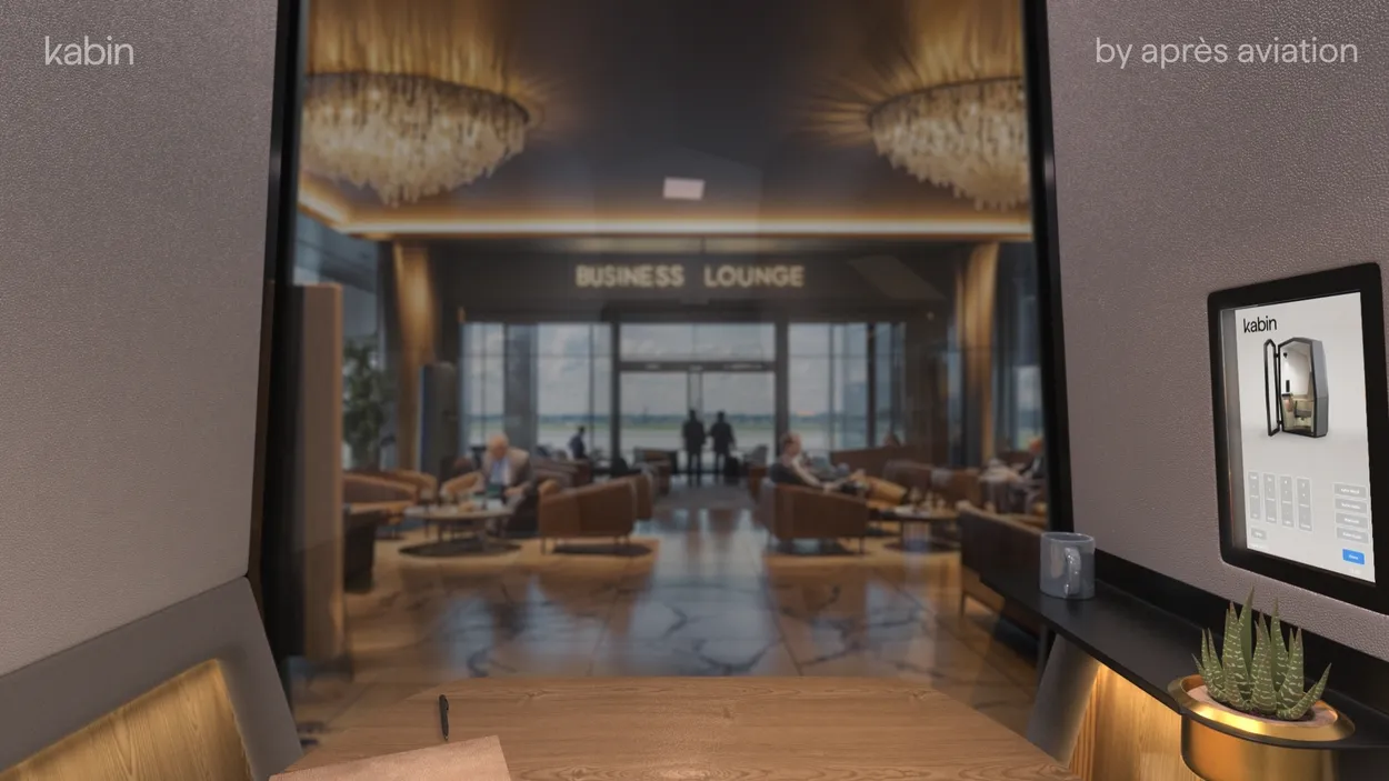 Vista en primera persona desde el interior de Kabin de Après Aviation, que muestra la disposición del escritorio privado y una vista despejada hacia una concurrida sala de negocios del aeropuerto.